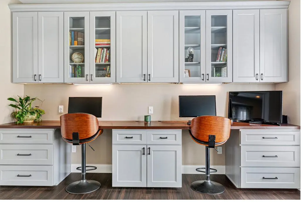 Completed custom home office built-ins with glass-door uppers and a wood desk top